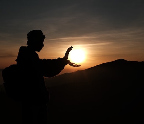 man framing, and appearing to push, the sun with the power of his hands and chi